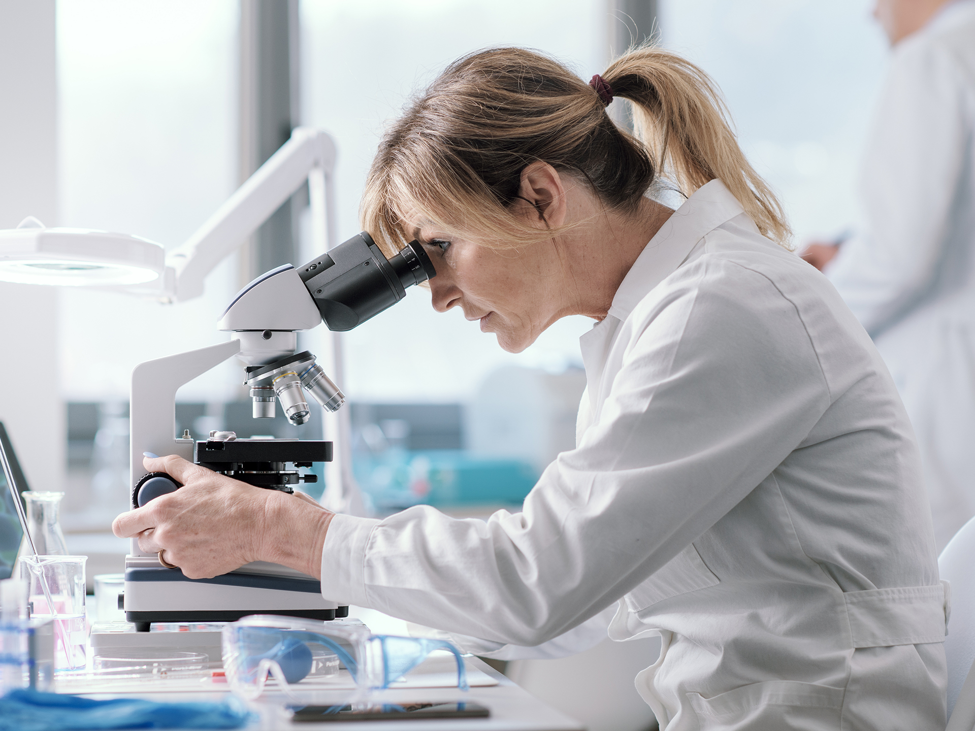 Forscherin mit weißem Kittel blickt in ein Mikroskop